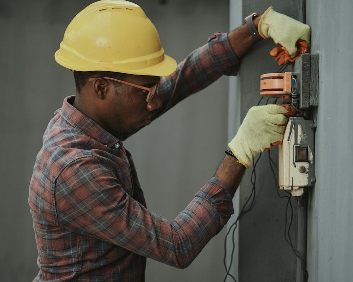 An electrician in a hard hat working on an electric meter