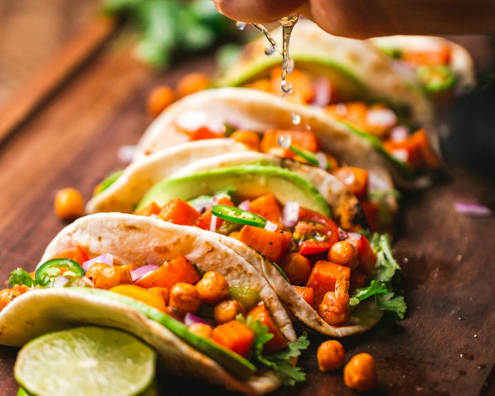 A hand squeezing lime over fresh tacos