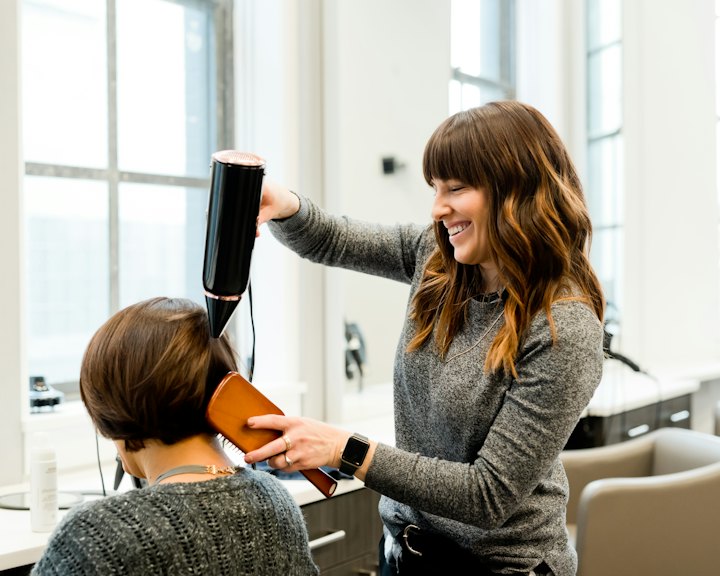 A stylist blow-drying a client's hair in a bright studio