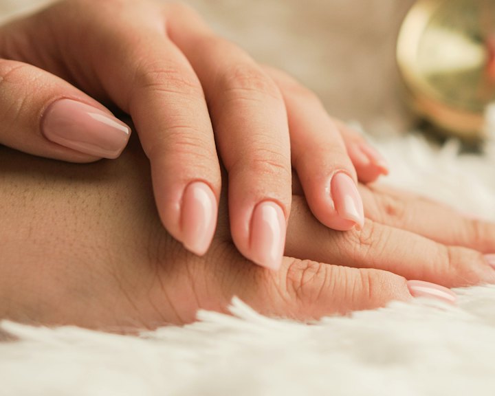 Hands with soft pink manicured nails resting on a cream throw