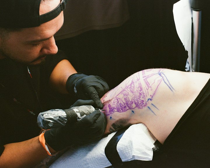 A tattoo artist in gloves working on a linework tattoo